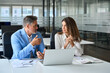 © insta_photos - Male executive manager explaining corporate project online strategy to female partner sitting at office desk. Business team of two busy professionals working together using laptop looking at computer.