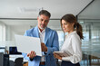 © insta_photos - Busy professional smiling businessman and businesswoman leaders having conversation at work. Executives team of two business people working talking using laptop technology standing in corporate office