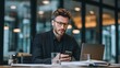 © Marius - Businessman in Glasses Using Smartphone While Working Intently in Modern Office Environment
