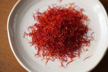 Poster - A bowl filled with red saffron threads on a wooden table.