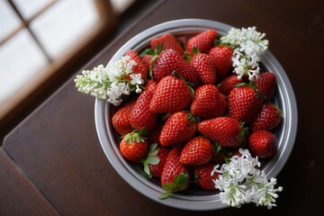 Poster - A bowl filled with red strawberries and white flowers on a wooden table.