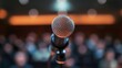 © Khan - A microphone stands on a stage in front of an audience.