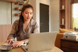 © snowing12 - Adult Asian woman working from home using a laptop for business and financial analysis in comfortable work environment