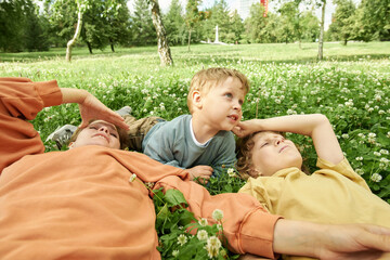 Wall Mural - Low angle view of family lying on green grass in park with focus on little boy looking away in sunlight