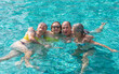 © luciano - Cheerful group of four mature relaxed friends having fun in outdoor swimming pool under the sun. Vacation and freedom in companionship, summer vibes concept