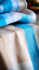 Poster - Folded textured blankets stack with blue and brown tones, fringe detail, warm lighting, soft textiles on dark wooden surface, cozy design elements