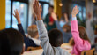 © Curioso.Photography - Group of schoolchildren raising their hands in a classroom during a lesson.