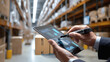 © MichaelMob - A person manages inventory using a digital tablet in a modern warehouse with shelves of boxes in the background.