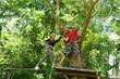 © romaset - A man and a woman is walking across a challenging ropes course in the extreme park