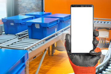 Poster - Phone near industrial conveyor. Production line in factory. Smartphone with white screen in hand. Phone template near conveyor. Place for delivery tracking app. Product delivery technology concept