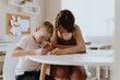 © looking2thesky - A loving mother and her son work together on homework at the kitchen table, symbolizing family support, education, and care. The scene highlights the importance of parental guidance