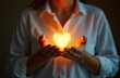 © Maryna - Person holds glowing heart symbol, representing inner light. Symbol of love, emotion, spirituality. Image focus on hands, heart. Symbolic representation of connection, warmth, tenderness, human