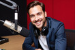© Alex & M Studio - male radio host, podcaster, or broadcaster with headphones smiles confidently into a professional microphone in a recording studio with soundproofing, embodying communication, media, entertainment