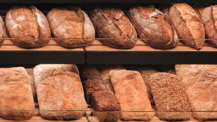 Poster - A variety of breads are displayed on shelves in a bakery. The breads are of different shapes and sizes, and they are arranged in a way that makes them easy to see and access