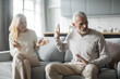 © Prostock-studio - A senior couple sits in a cozy living room, engaged in a heated discussion. The woman gestures expressively while the man appears defensive, highlighting their communication struggles.