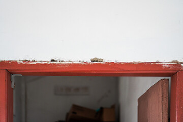 Poster - A vintage red door frame contrasts with a bright white wall, adding a touch of rustic charm. This unique architectural detail offers a glimpse into a partially opened door creating depth and intrigue.