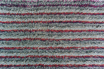 Poster - Detailed close-up of a striped, woven rug displaying a pattern of gray, red, and pink lines. The texture is rough and plush, creating a cozy and inviting feeling with its detailed design.