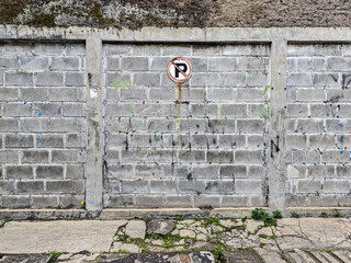 Poster - An urban scene featuring an aged brick wall, divided by concrete pillars and topped with a textured surface. A 'no parking' sign adds character, emphasizing textures and decay.