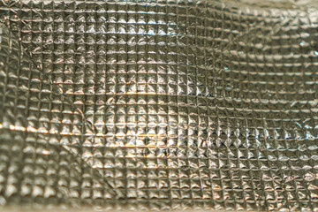 Poster - Abstract close-up of a shiny, metallic surface with a textured, geometric pattern. The material's reflective properties create dynamic light and shadow, adding depth and visual interest.