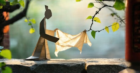 Aufkleber - Paper figure hangs laundry. Sunlight filters through leaves, creating soft shadows. Minimalist scene evokes quiet domesticity.