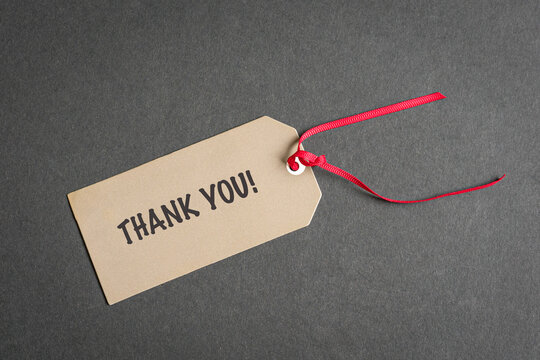 Thank you tag with red ribbon. On top of dark surface. High angle view.