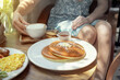© Vladimir Razgulyaev - Delicious pancakes served with coffee and syrup in a cozy cafe setting. A woman in the background drinks cappuccino coffee, summer cafe in the sunshine, outdoor breakfast