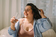 © Tatyana - A positive young curly-haired plus-size woman drinks water after waking up in bed.Healthy lifestyle.