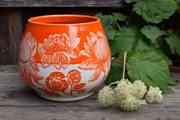 Poster - Vibrant hand-painted pottery bowl surrounded by greenery on rustic wooden surface in natural light