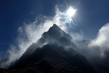 Poster - Majestic mountain peak surrounded by clouds and sunlight in a clear blue sky at midday