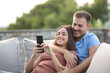 © Antonioguillem - Happy couple smiling checking mobile phone in a terrace