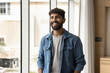 © fizkes - Successful and satisfied. Cheerful candid millennial male in stylish youth closing stand near window at modern office. Happy young student enjoy good day at university. Smiling employee feel motivated