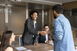 © fizkes - Warm welcome. Happy young man office coworker start new company career get acquainted to friendly diverse corporate team department staff on daily briefing shake hand introducing to smiling HR partner