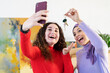 © Studio Marmellata - Two excited young women, one wearing a hijab, take a selfie while holding up keys. They are celebrating a significant purchase or new property acquisition.