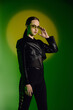© LIGHTFIELD STUDIOS - Stylish young woman poses confidently in black attire against vibrant green backdrop