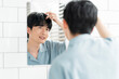 © lielos - メンズビューティー /ヘアケア /鏡を見ながら髪を触っている若い日本人男性。