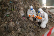 © BESTIMAGE - Two workers in protective suits masks gloves and coveralls collecting hazardous waste or trash in an outdoor urban environment with debris and rocky surface under a bridge or structure