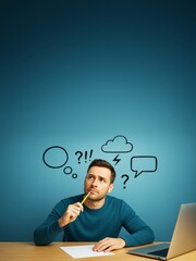 Poster - Thoughtful man with pencil sitting at desk looking up with doodle symbols above head on blue background, ideal for business concept banners.