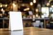 © Aisyaqilumar - A blank, white menu card stands on a shiny wooden table in a blurred restaurant setting.