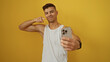 © Krakenimages.com - Young hispanic man posing confidently with smartphone against isolated yellow background, showcasing modern self-expression and technology.