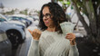 © Krakenimages.com - Middle-aged woman outdoors in the uae city holds dirham banknotes looking puzzled pointing side on street.
