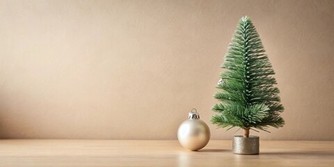 Poster - A single silver ornament rests beside a miniature flocked Christmas tree on a wood surface against a beige backdrop.