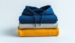 © SS Studio - A stack of folded clothing featuring a blue hoodie a gray sweater and a yellow shirt on a white background