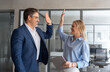 © Stock 4 You - Happy smiling successful Hispanic businessman and young European professional business woman celebrating achieving superior performance, outcomes in work giving high five standing in office workspace.