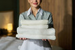 © pressmaster - Portrait of smiling hotel attendant holding stack of fresh towels. Warm, inviting environment in background, suggesting welcoming service