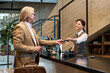 © pressmaster - Professional setting with businessman handing ID card to smiling receptionist at modern office reception desk, conducting check-in process