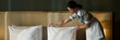 © pressmaster - Housekeeping staff member preparing bed linens in an elegant, cozy hotel room with meticulous attention to detail, ensuring a comfortable stay for guests