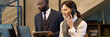 © pressmaster - Two business professionals analyzing data on digital devices while standing in modern office. Man wearing suit using tablet, woman speaking on phone