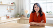 © Prostock-studio - A woman sits at a kitchen counter, engaged in facial recognition technology. The sunlight illuminates her features, highlighting the blend of comfort and advanced technology in daily life.