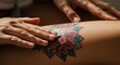 © Richafuji - Close-up of a person's hand applying cream to a vibrant floral tattoo on the leg. Focus on skin care, body art, and a detailed, colorful design.
