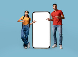 Poster - Mobile Offer. Cheerful Arab Couple Pointing At Big Cellphone With White Screen For Mockup, Happy Middle Eastern Man And Woman Demonstrating Copy Space For Phone Application Design, Blue Background